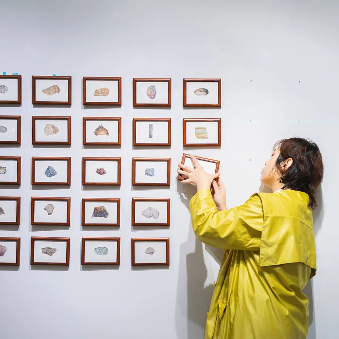 Student adjusts framed rock and mineral specimens on a gallery wall during a museum exhibition installation.
