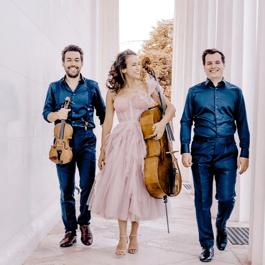 Two men and a woman walk along a marble colonnade 