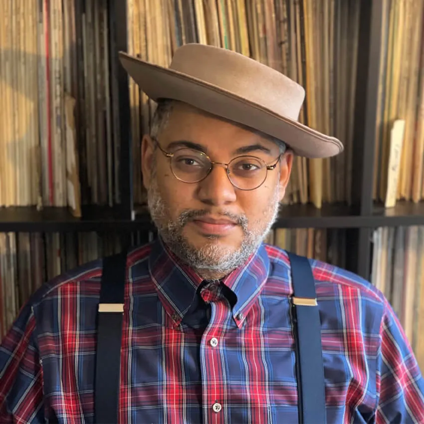 A man in a plaid shirt in front of shelves containing vinyl records