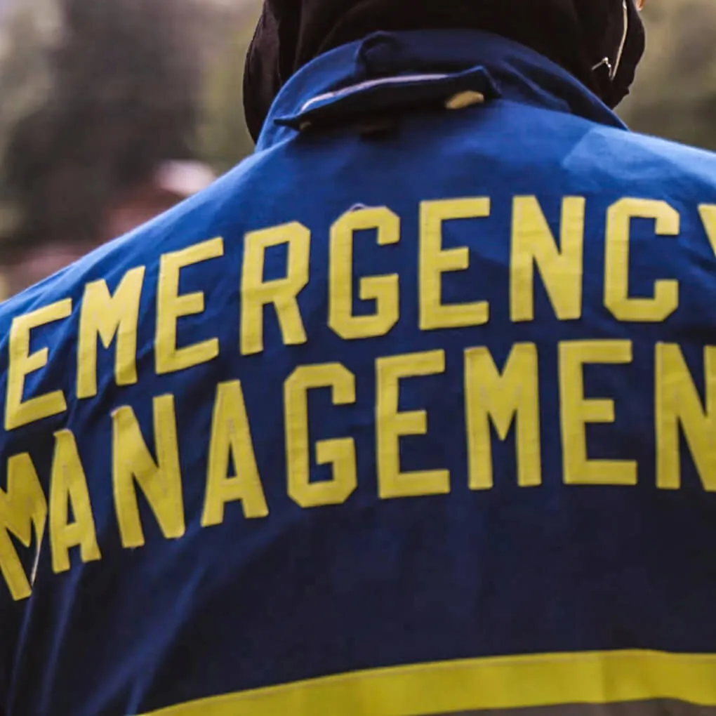 Photo of the back of a blue jacket with a yellow stripe. Yellow letters say "Emergency Management".