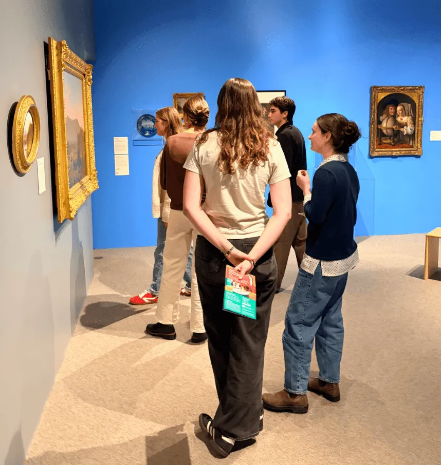 A small group of college students stand in front of a large painting on a blue wall.