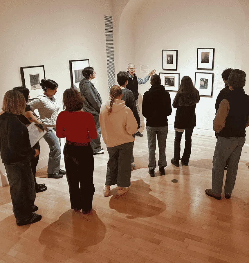UVM faculty gestures to a photograph on the wall as a group of students consider the work.