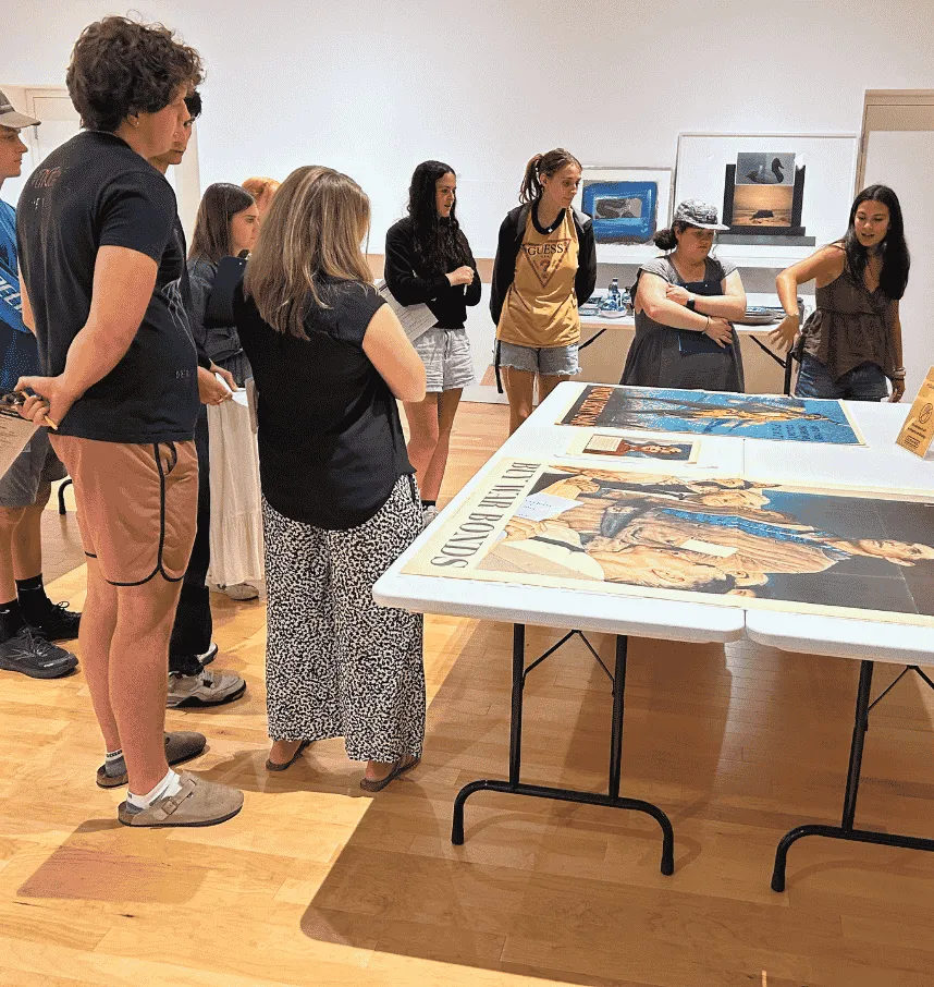 A group of students gathers around a table to look closely at large posters.