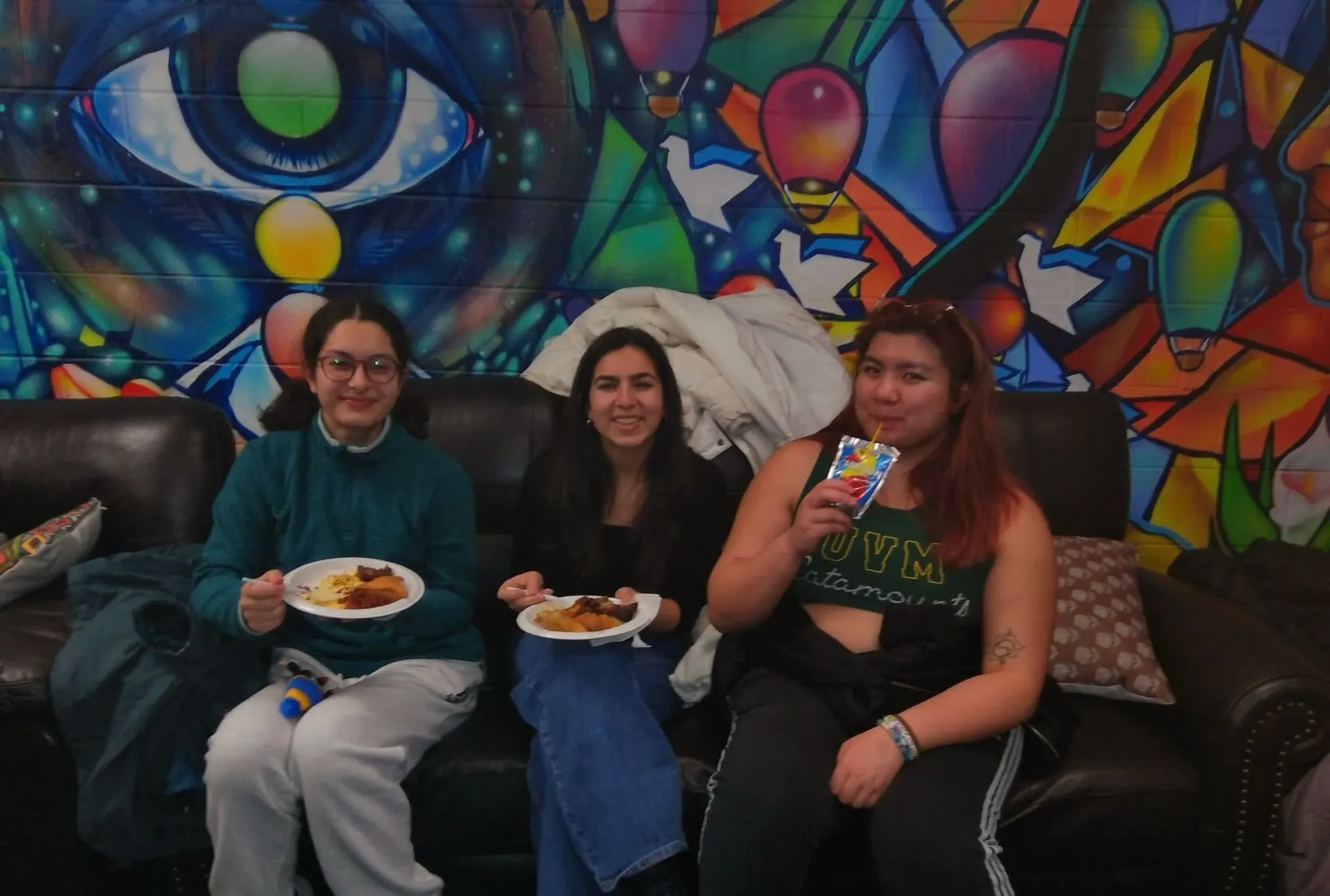 Students enjoying foods while sitting in front of the Mosaic mural 