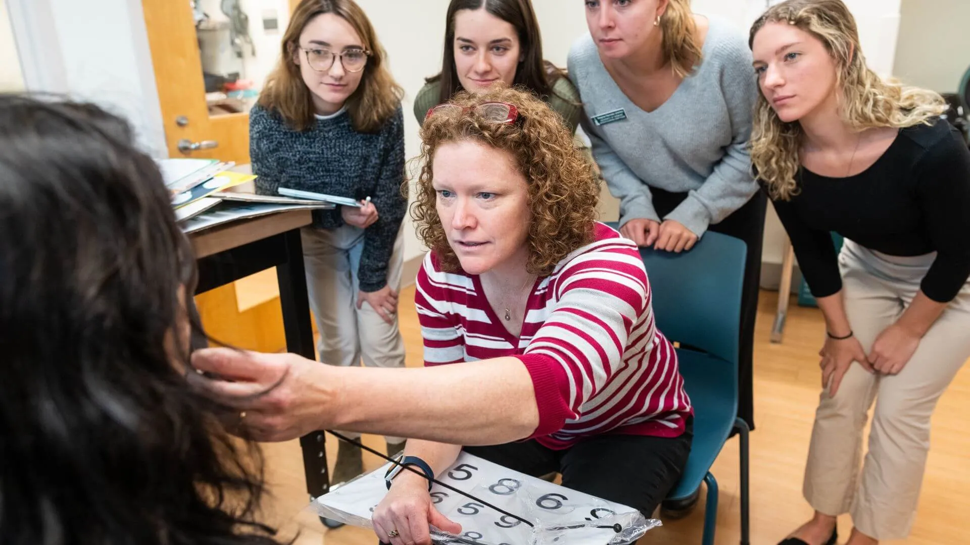 Instructor demonstrates a clinical assessment technique while students observe in a classroom setting.