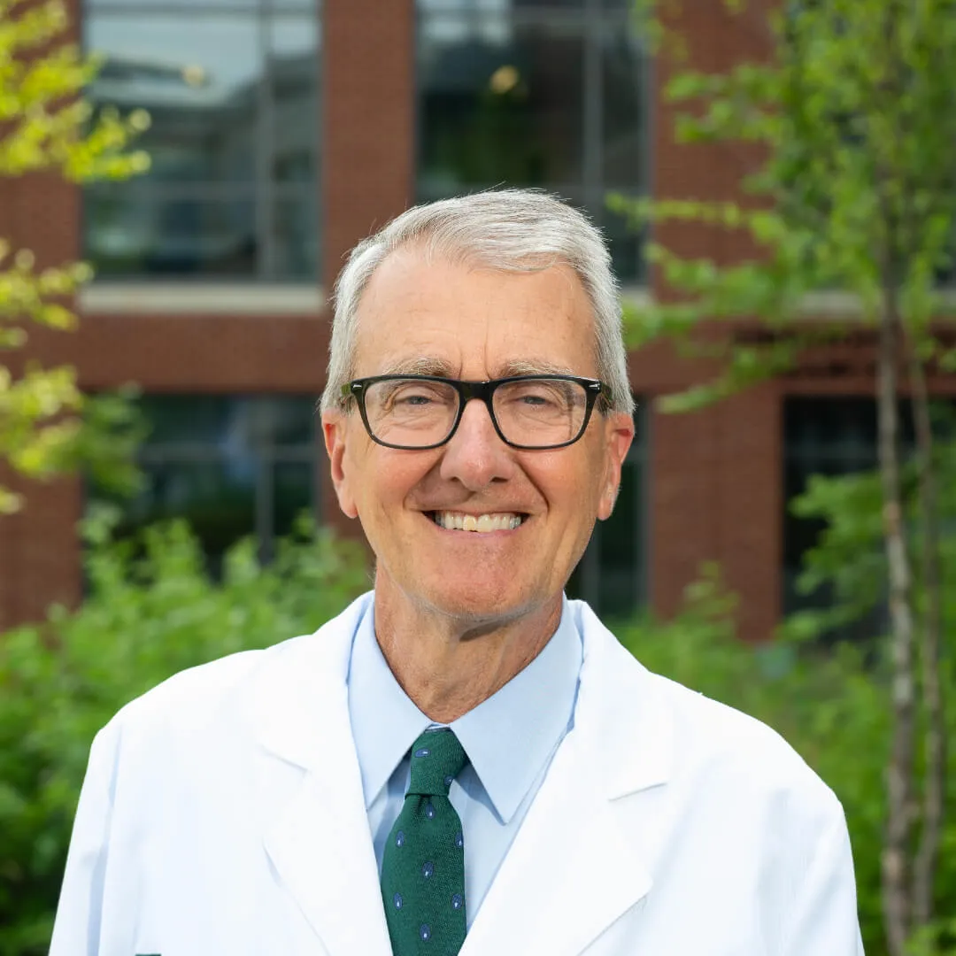 light skinned man with short gray hair and glasses wearing a white doctors coat