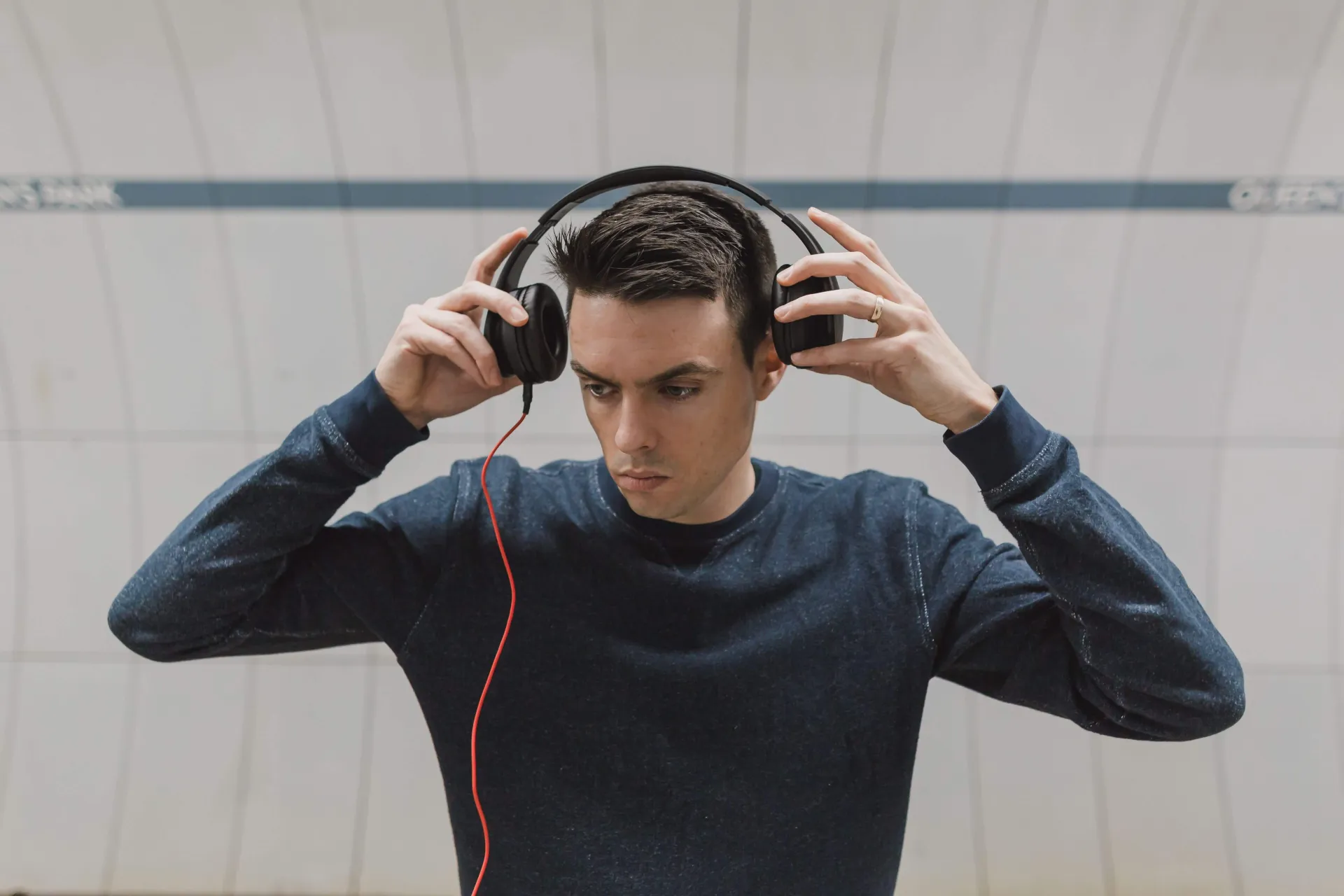 Pale-skinned college-aged boy in dark sweater puts on headphones while looking off-screen
