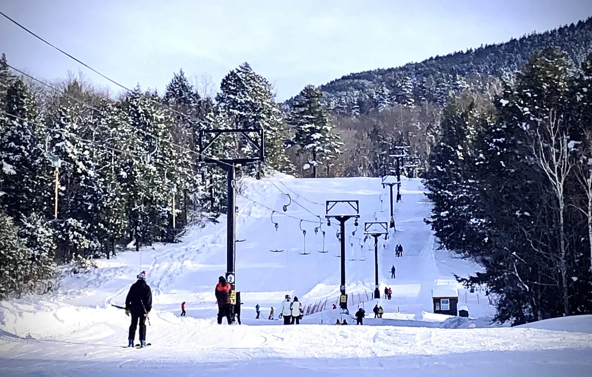 A group of people on a ski lift with a ski area in the background.