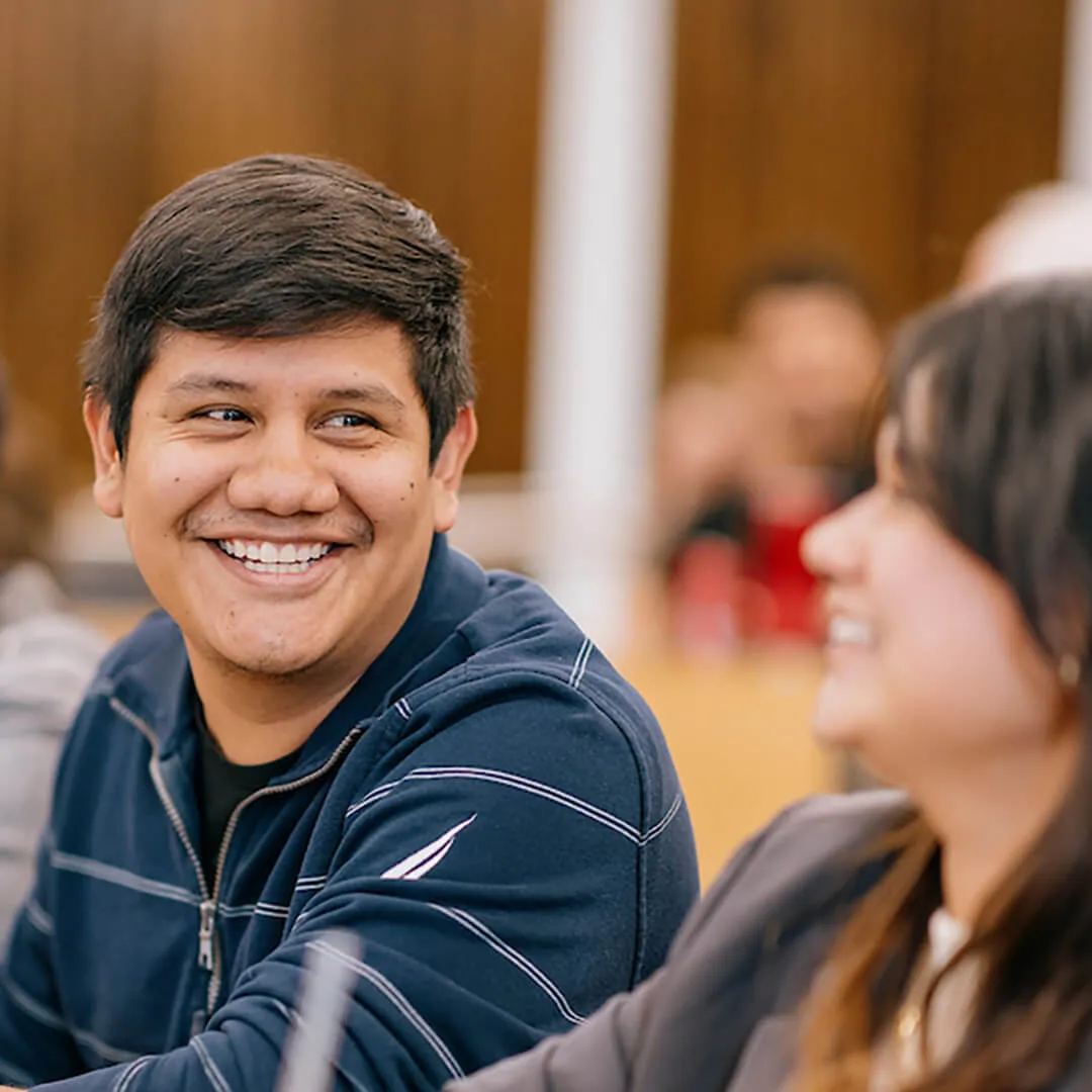 Two people smiling and talking indoors.