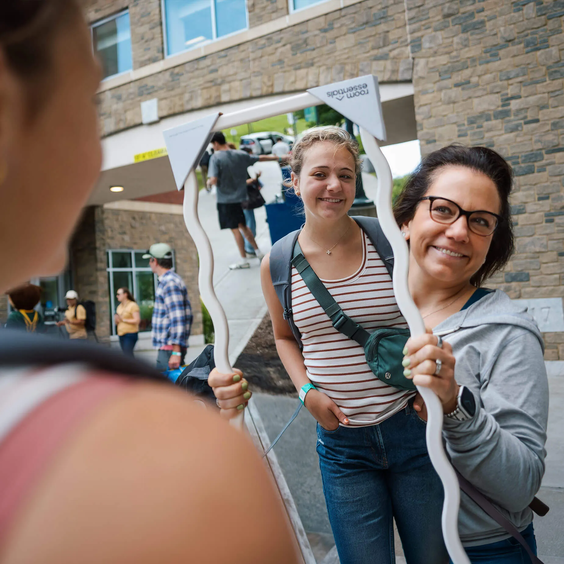 a mother holds up a mirror reflecting the image of their student in front of a brick building
