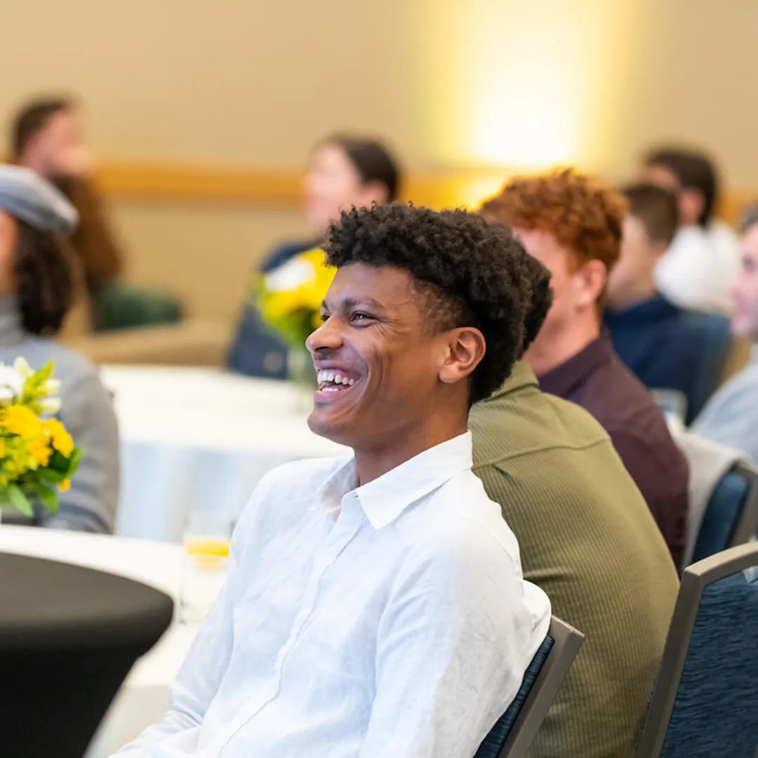 Person smiling while seated at an indoor event.