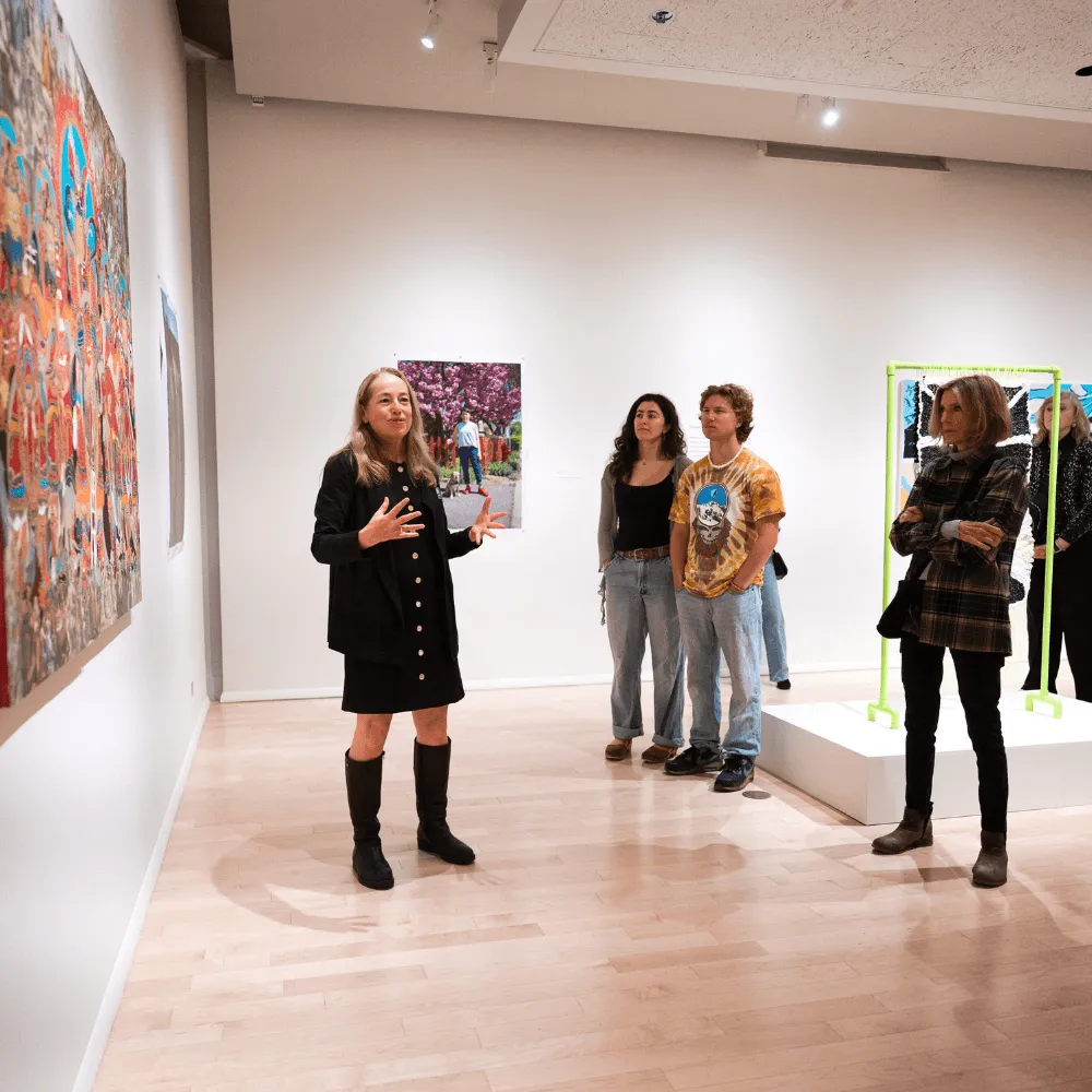 A woman standing in front of a painting, gesturing to the museum visitors.