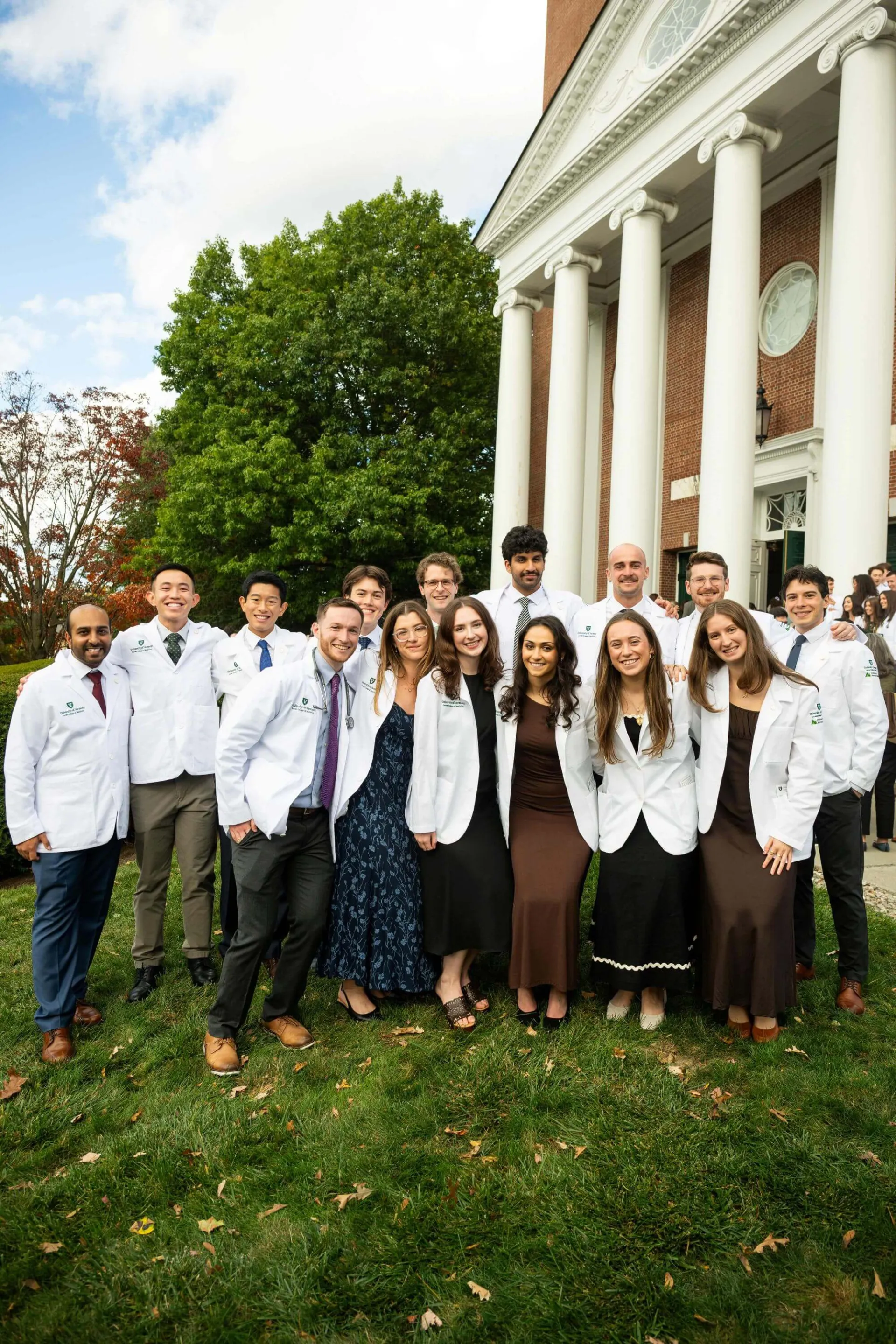Group in white medical coats posing outside a brick building with tall white columns.