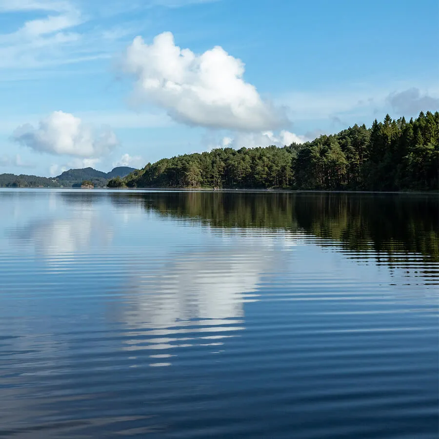 a large lake reflecting blue sky and white clouds, with gentle green hills hugging the shore