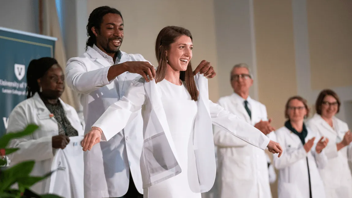 Class of 2028 medical student Caroline Donohue receives her white coat on the stage in UVM's Ira Allen Chapel from Tony Williams, M.D., assistant professor of family medicine and assistant dean of admissions.