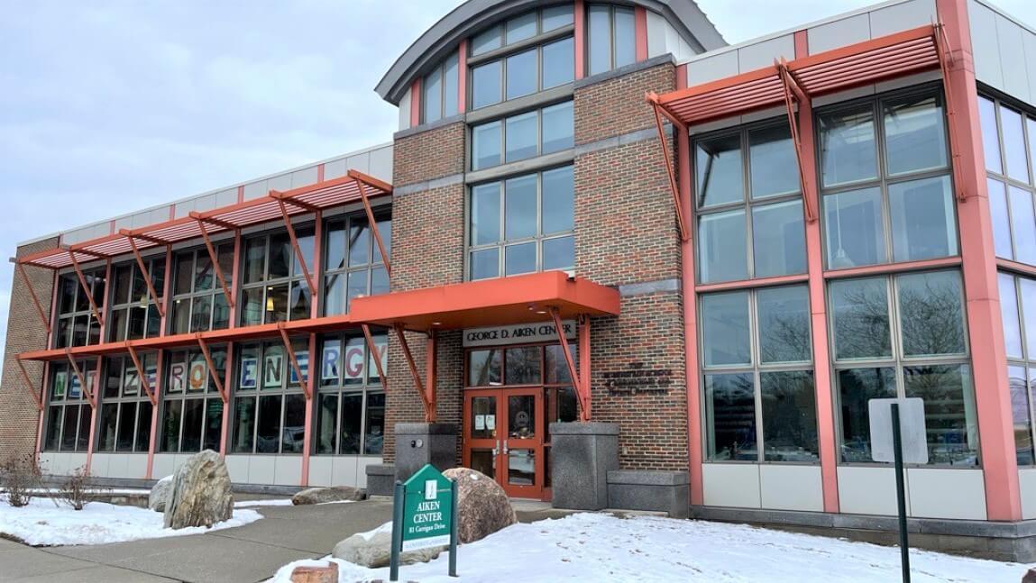 The front of the Aiken Center with snow on the ground and signs spelling out "Net Zero" in the windows