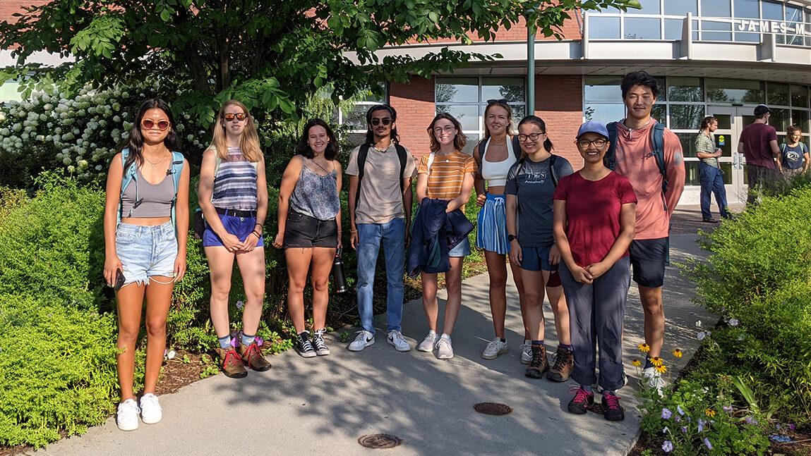 Eight undergraduate scholars and their leader in front of campus building