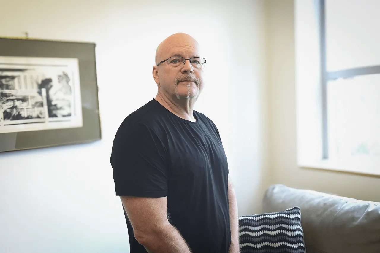 Man in black t-shirt with a goatee in a conference room