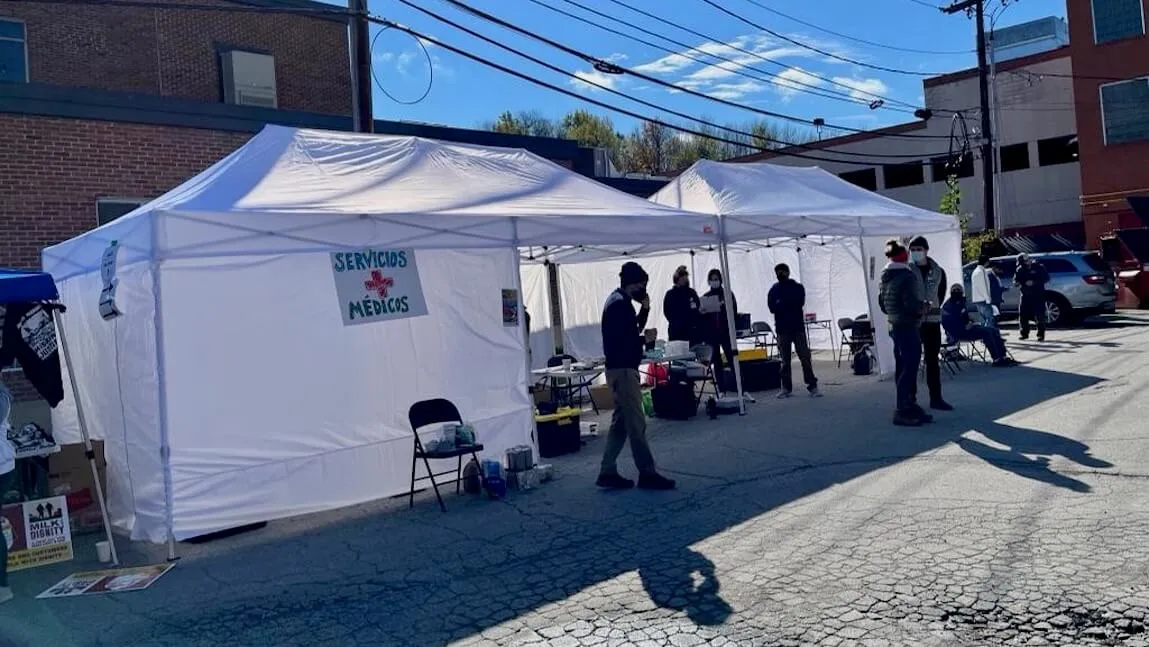 white tents with tables and health care workers are set up in a downtown street with the sign reading "servicos médicos".