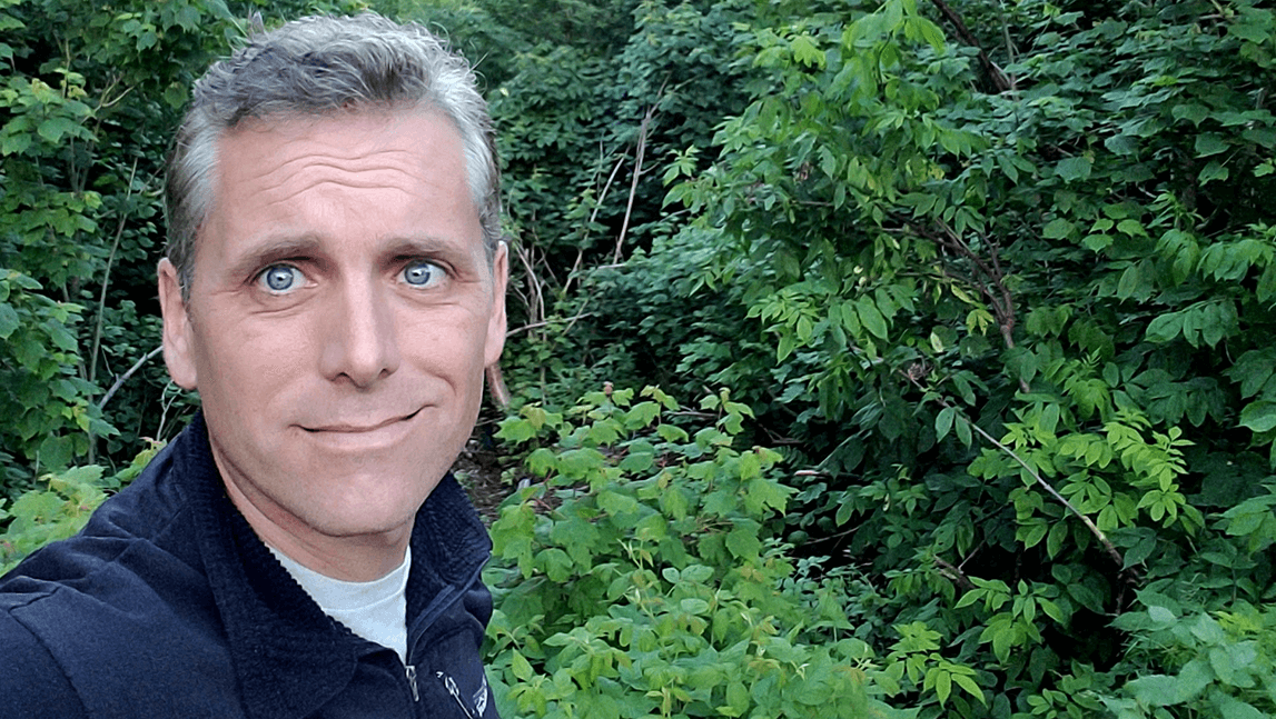 Bradley Bauerly selfie with green foliage in the background, a smile on his face