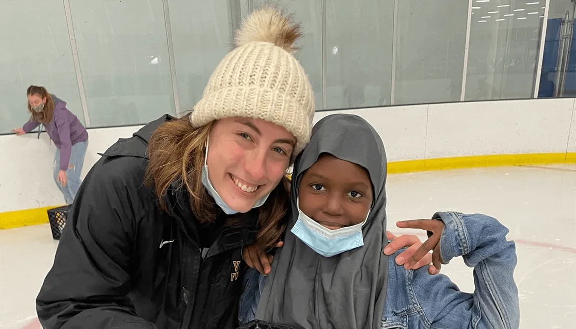 Rebekah Silver and young black girl dressed for cold weather posing with smiles at an ice skating rink.