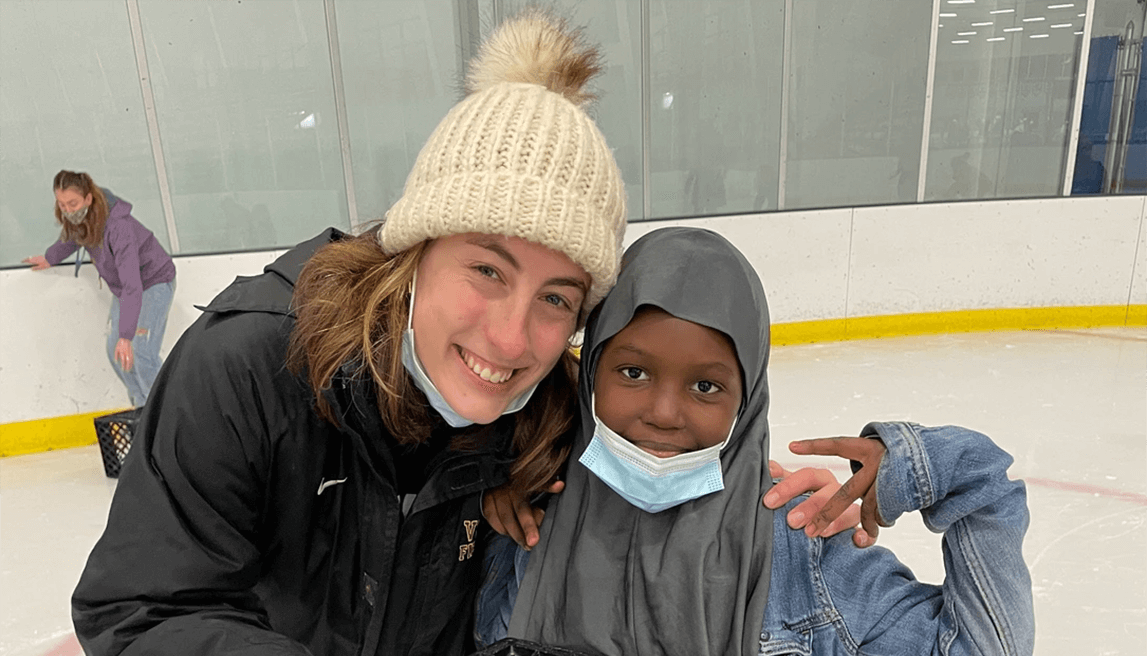 Rebekah Silver and young black girl dressed for cold weather posing with smiles at an ice skating rink.