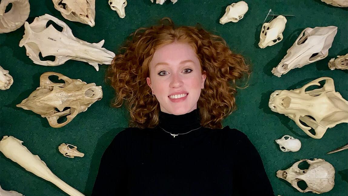 red head lying back on a green background with skulls surrounding