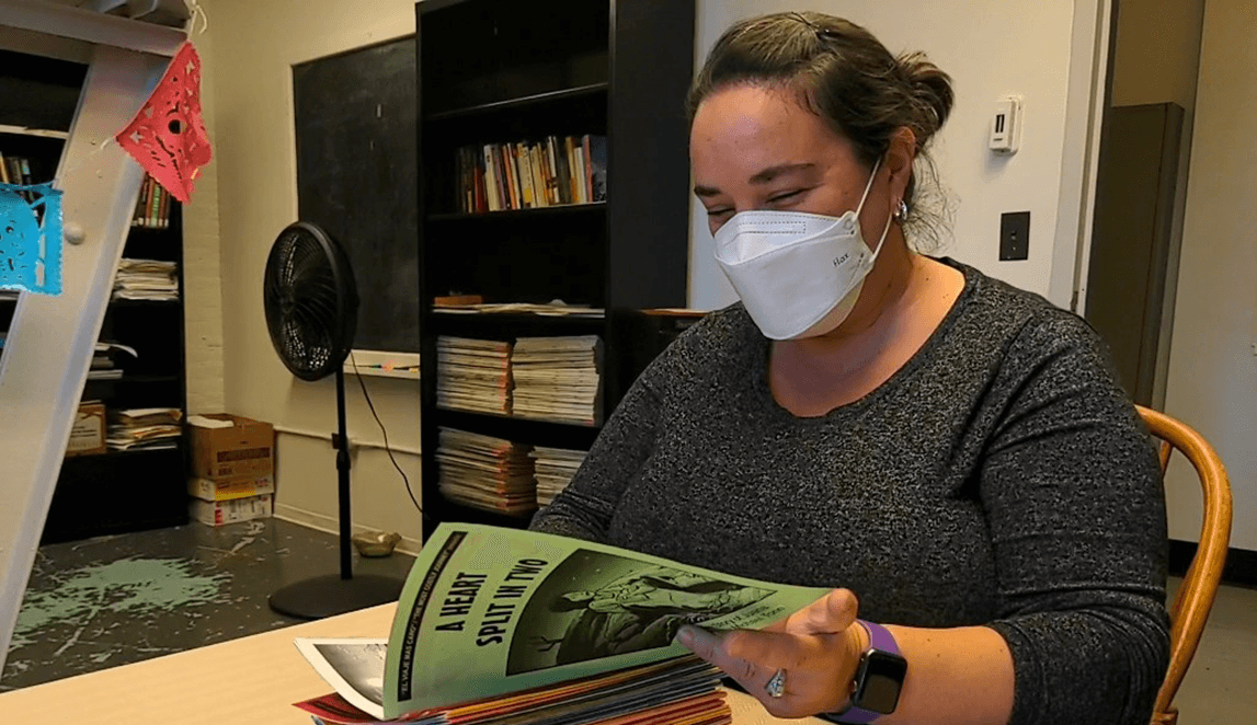 Teresa Mares sits at a desk in her office looking through Spanish comic books