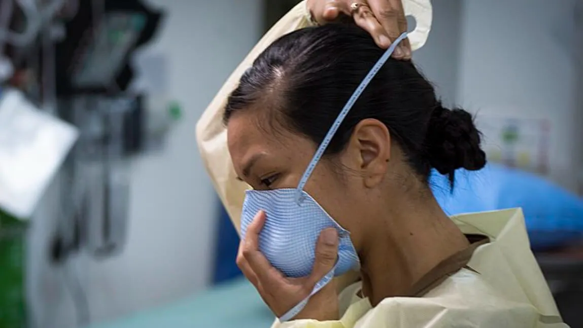 Person wearing nursing scrubs putting a personal protective mask on their face with worried expression