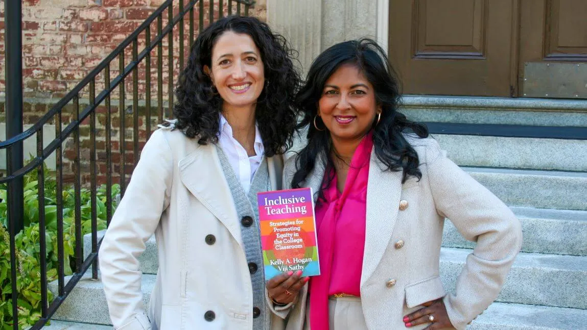 Kelly Hogan and Viji Sathy pose in front of a brick building with their book, Inclusive Teaching, held between them