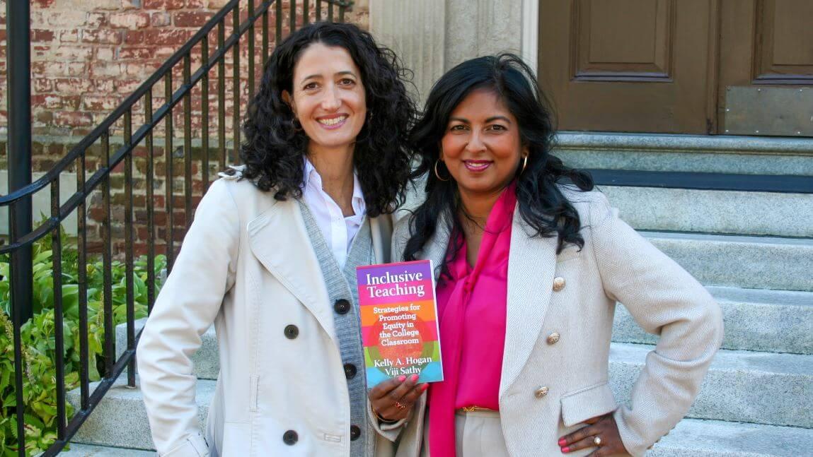Kelly Hogan and Viji Sathy pose in front of a brick building with their book, Inclusive Teaching, held between them