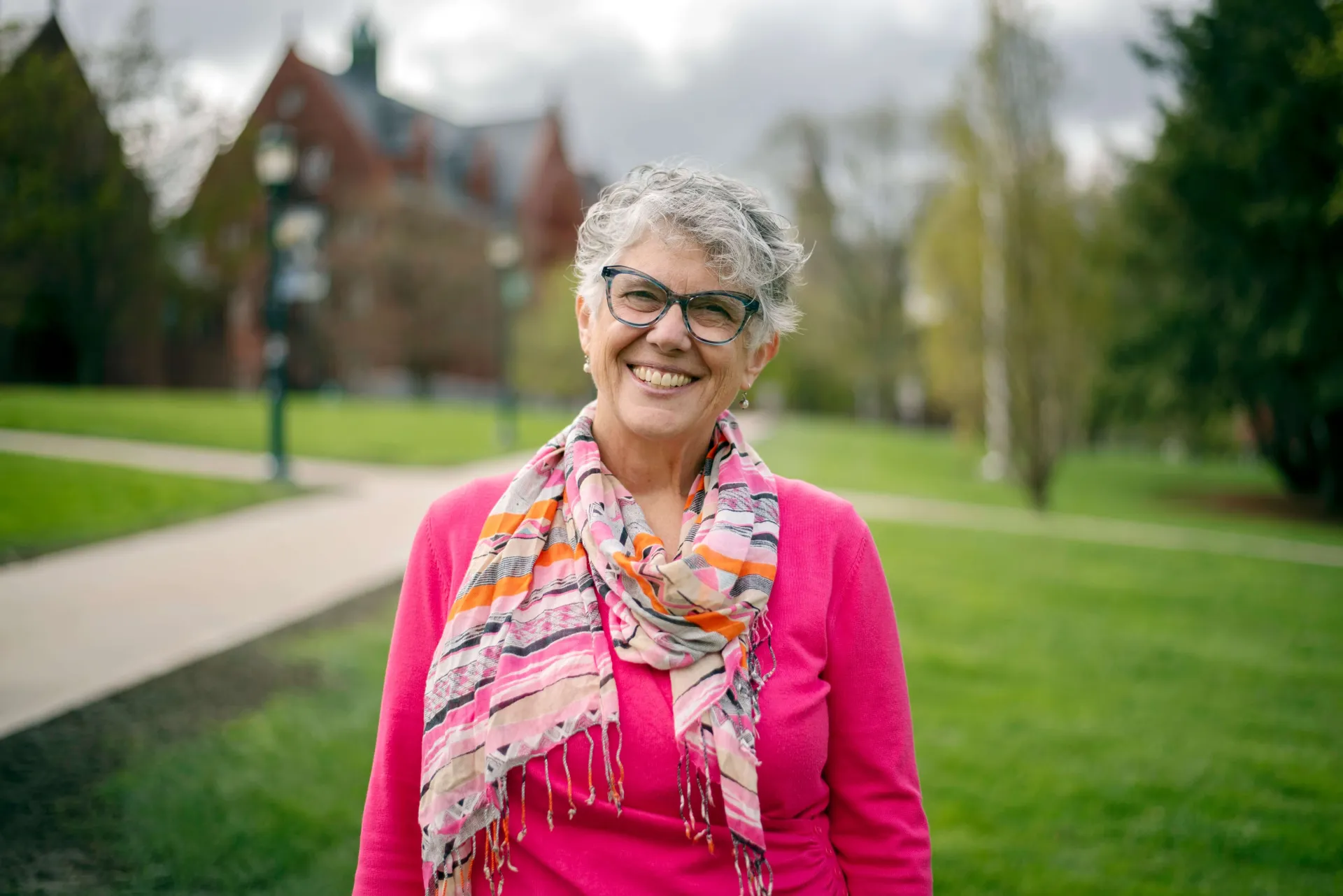 Dr. Sharon Glezen, a white woman with gray hair, smiles for the camera wearing a bright pink blouse and colorful scarf.