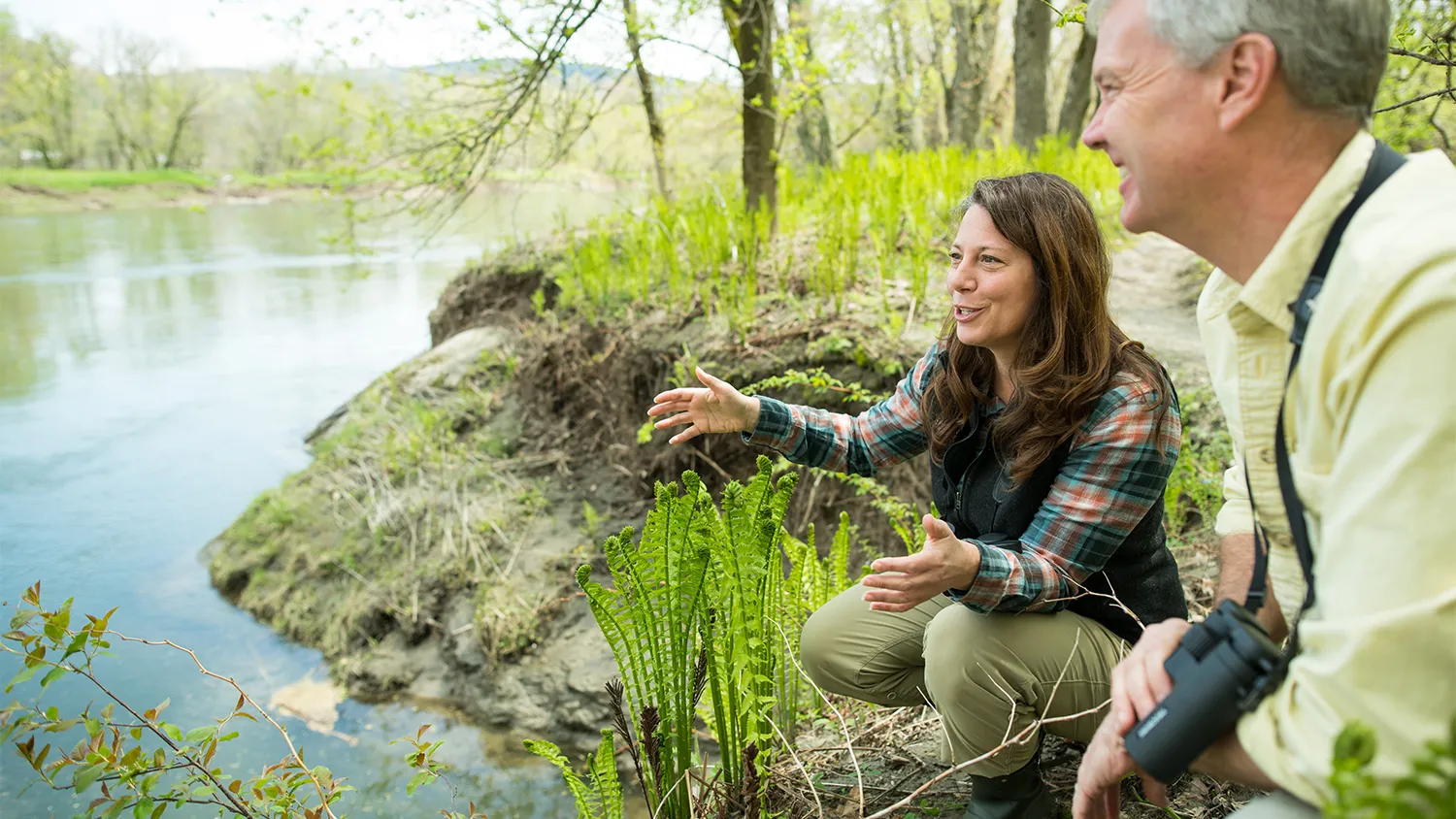 Two researchers crouch along a riverbank in Richmond, Vermont.