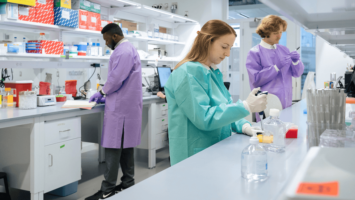 Three people in PPE work in a lab setting