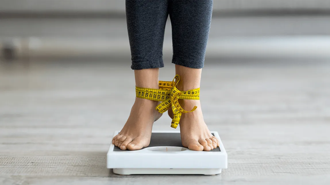 bare feet tied together with a measuring tape standing on a scale