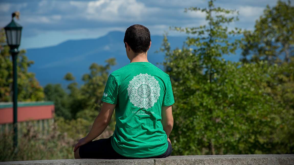 back of male sitting in yoga pose overlooking the mountain view