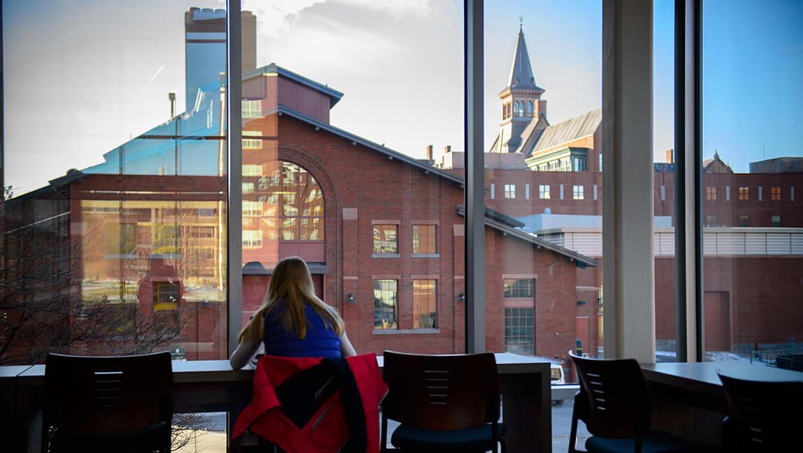 student at desk in front of window overlooking campus