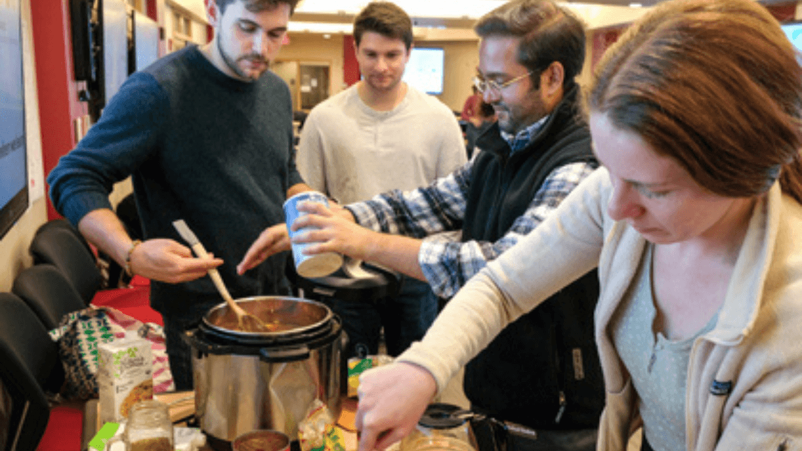 Four people standing around a buffet of food and reaching for healthy food items