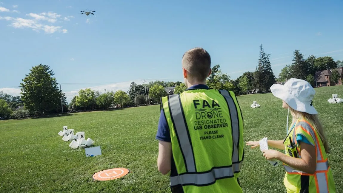 A participant in the UVM drone training workshop being led through a flight training proficiency test outside on a campus green.