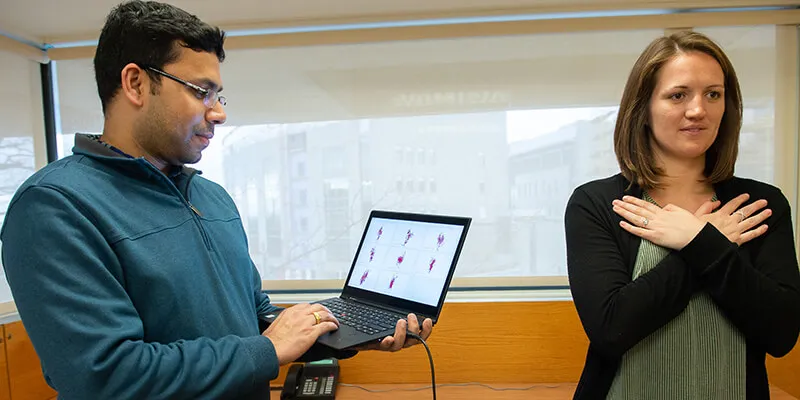 Professor Mohapatra holds a laptop next to a student standing with her arms crossed, demonstrating concussion screening test.