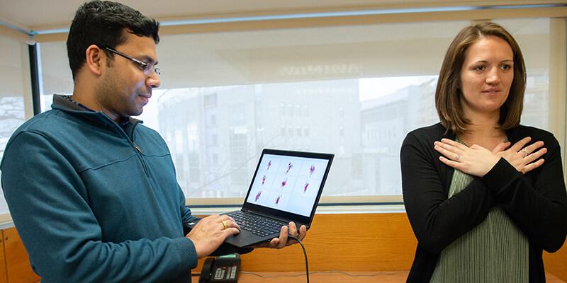 Professor Mohapatra holds a laptop next to a student standing with her arms crossed, demonstrating concussion screening test.