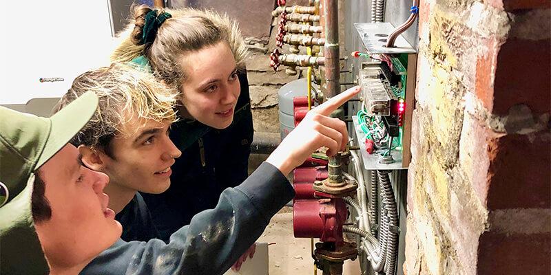 Three students looking at electrical unit in basement