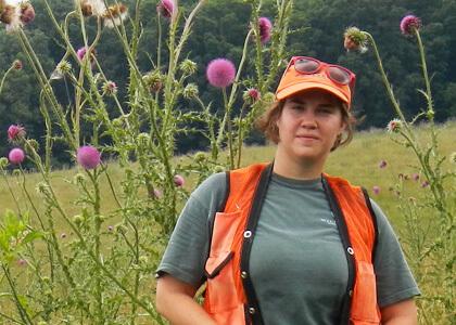 Alea Tuttle standing in a North Carolina pasture next to an introduced invasive called "musk thistle."