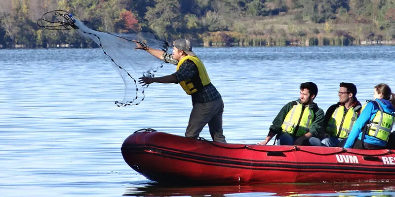 Student in boat tossing net on Shelburne Pond