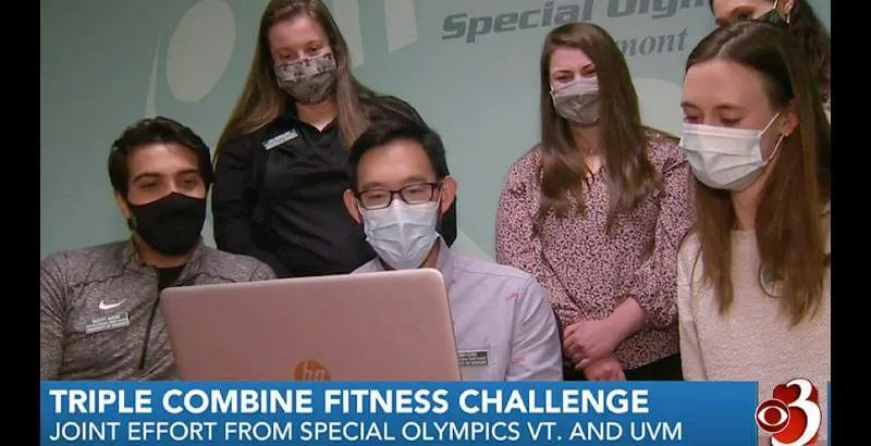 Six graduate students wearing masks gathered together looking at a computer screen