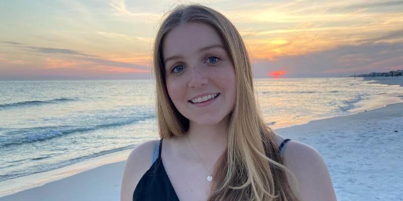 Emily Dow smiling at the camera, with a background of a sunset over a lake