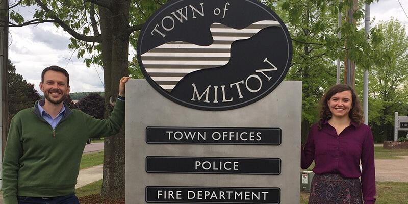 Student and town official stand next to Town of Milton sign