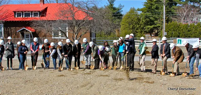 Suits in hardhats wielding golden painted shovels.