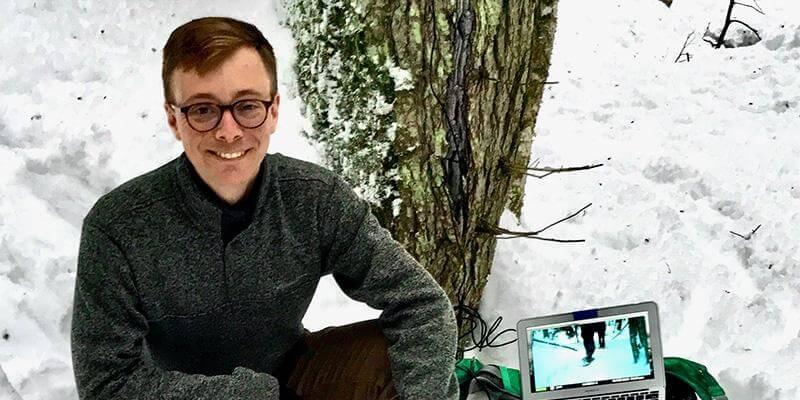 Joshua Morse kneels in snowy woods with his laptop computer