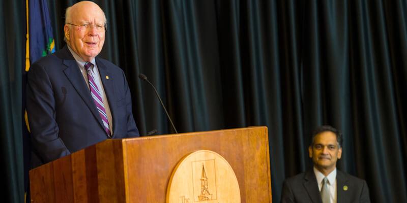 Senator Patrick Leahy speaks at a podium on stage with Suresh Garimella at the University of Vermont